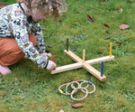 A child kneeling down setting up the Wooden Story Ring Toss Game on grass. The child is putting the red coloured post in place. 