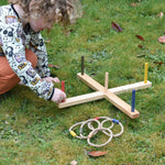 A child kneeling down setting up the Wooden Story Ring Toss Game on grass. The child is putting the red coloured post in place. 