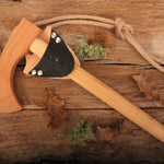 vah wooden toy battle axe pictured on a wooden surface with leaves and pieces of moss around it