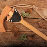vah wooden toy battle axe pictured on a wooden surface with leaves and pieces of moss around it