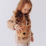 A child wearing the Wooly Organic Kids' Teddy Bear Crossbody Bag. The classic Wooly Organic bear turned into a cute wearable bag for children. A range of Wooly Organic bears and clothing are available at Babipur.