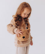 A child wearing the Wooly Organic Kids' Teddy Bear Crossbody Bag. The classic Wooly Organic bear turned into a cute wearable bag for children. A range of Wooly Organic bears and clothing are available at Babipur.