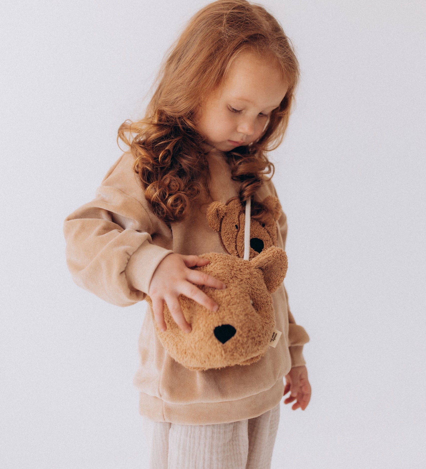 A child wearing the Wooly Organic Kids' Teddy Bear Crossbody Bag. The classic Wooly Organic bear turned into a cute wearable bag for children. A range of Wooly Organic bears and clothing are available at Babipur.