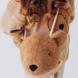 A close up of a Wooly Organic Kids' Teddy Bear Crossbody Bag being worn by a child. The classic Wooly Organic bear turned into a cute wearable bag for children. A range of Wooly Organic bears and clothing are available at Babipur.