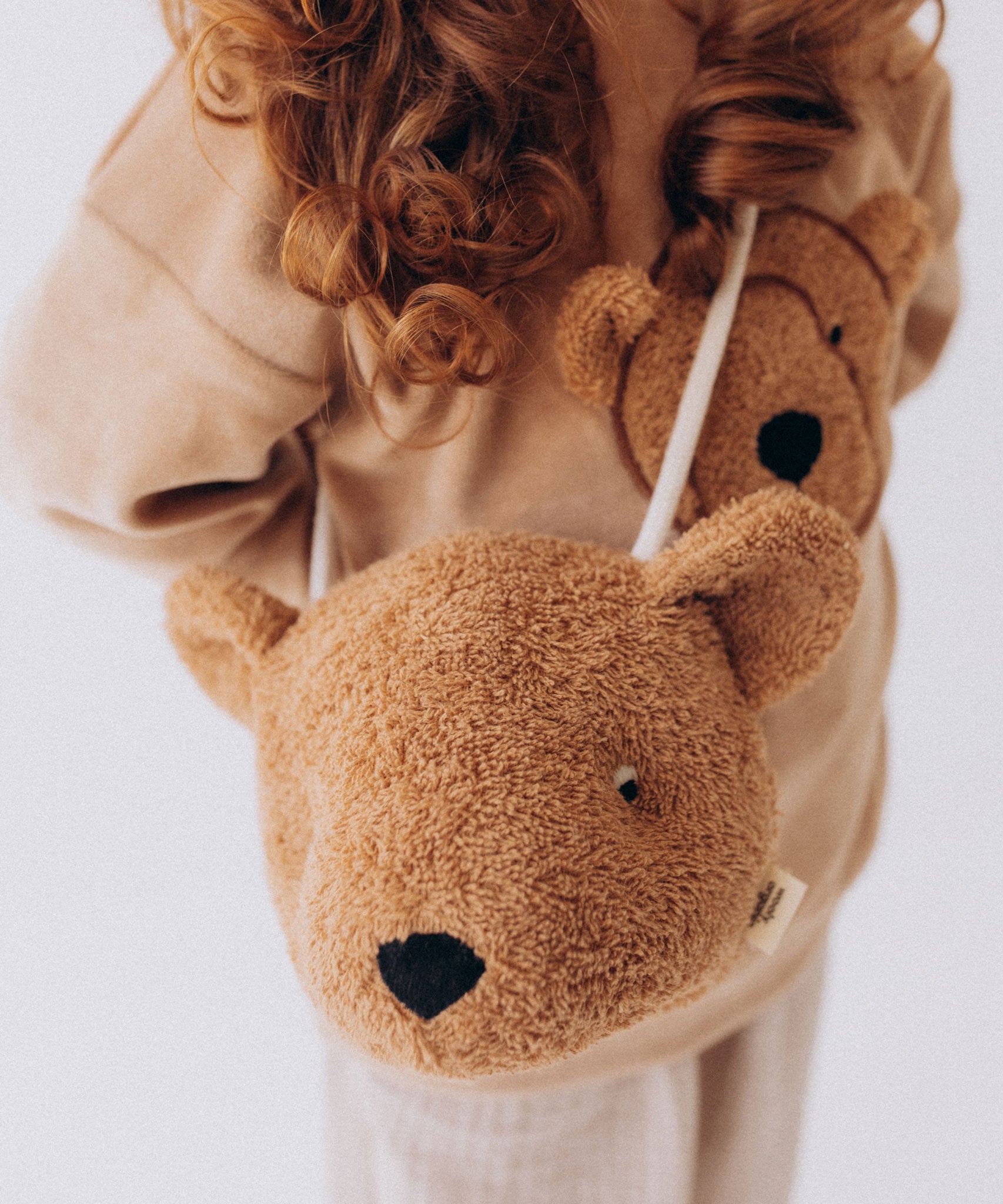 A close up of a Wooly Organic Kids' Teddy Bear Crossbody Bag being worn by a child. The classic Wooly Organic bear turned into a cute wearable bag for children. A range of Wooly Organic bears and clothing are available at Babipur.
