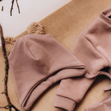 A decorative flatlay showing the  Wooly Organic hat with teddy ears in pale blush / savannah available at Babipur on top of the old pink sweater