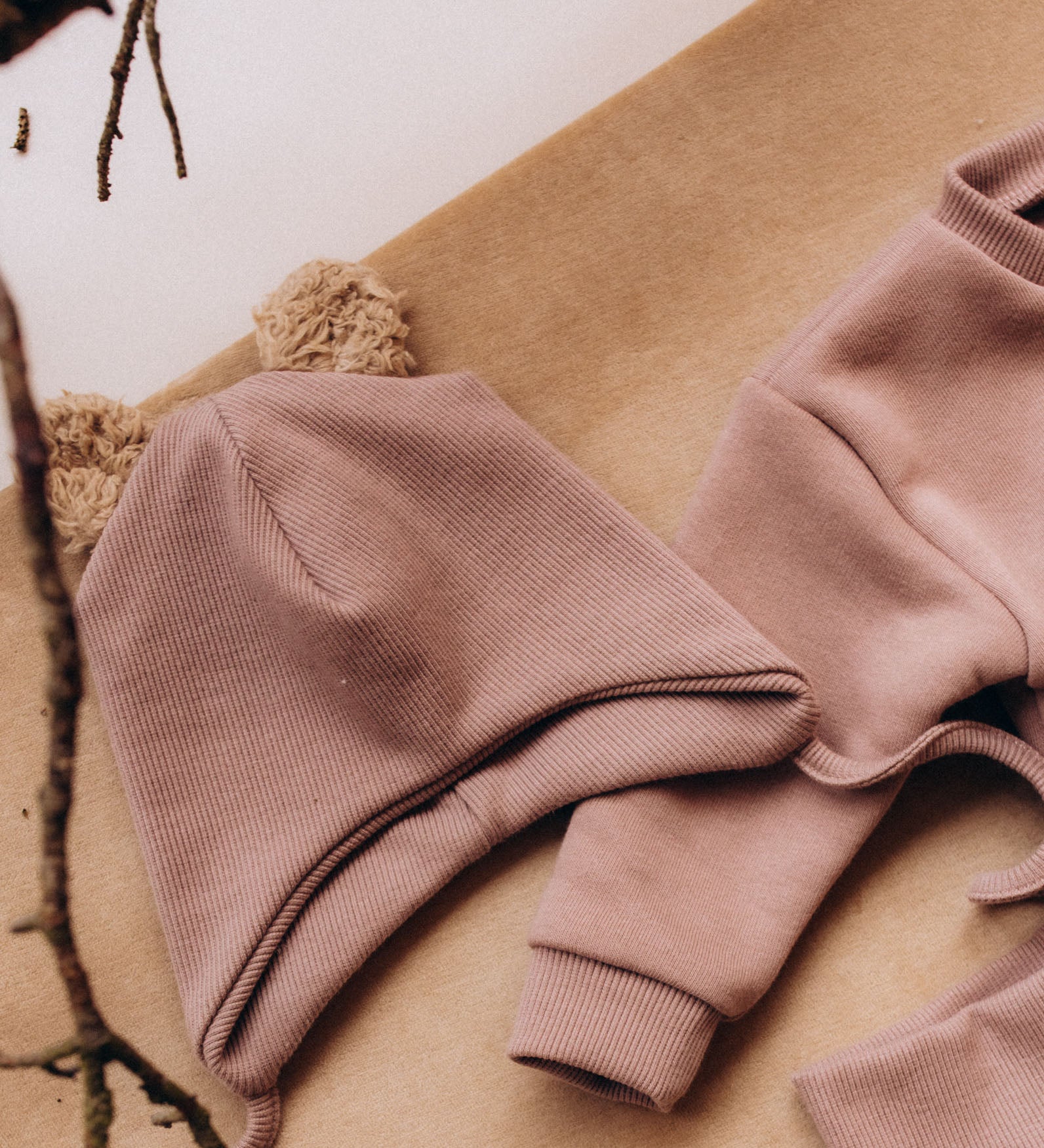 A decorative flatlay showing the  Wooly Organic hat with teddy ears in pale blush / savannah available at Babipur on top of the old pink sweater