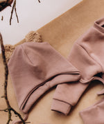 A decorative flatlay showing the  Wooly Organic hat with teddy ears in pale blush / savannah available at Babipur on top of the old pink sweater