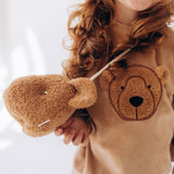 A child wearing the Wooly Organic Kids' Teddy Bear Crossbody Bag. The classic Wooly Organic bear turned into a cute wearable bag for children. A range of Wooly Organic bears and clothing are available at Babipur.