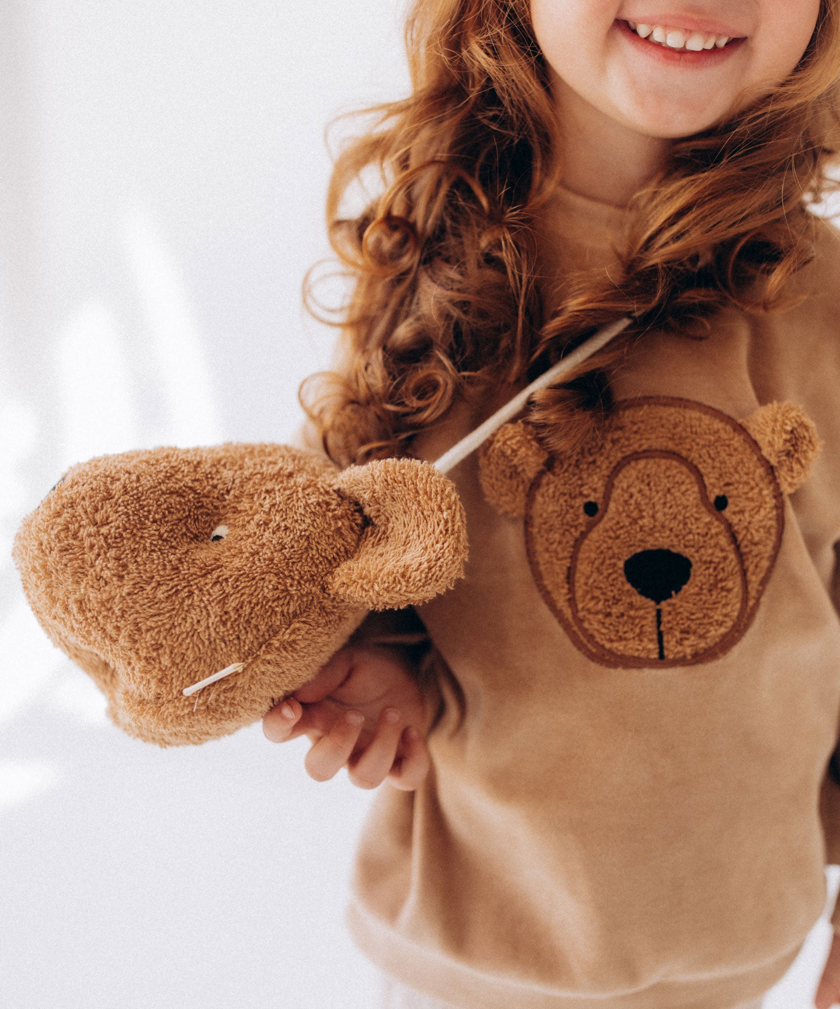 A child wearing the Wooly Organic Kids' Teddy Bear Crossbody Bag. The classic Wooly Organic bear turned into a cute wearable bag for children. A range of Wooly Organic bears and clothing are available at Babipur.