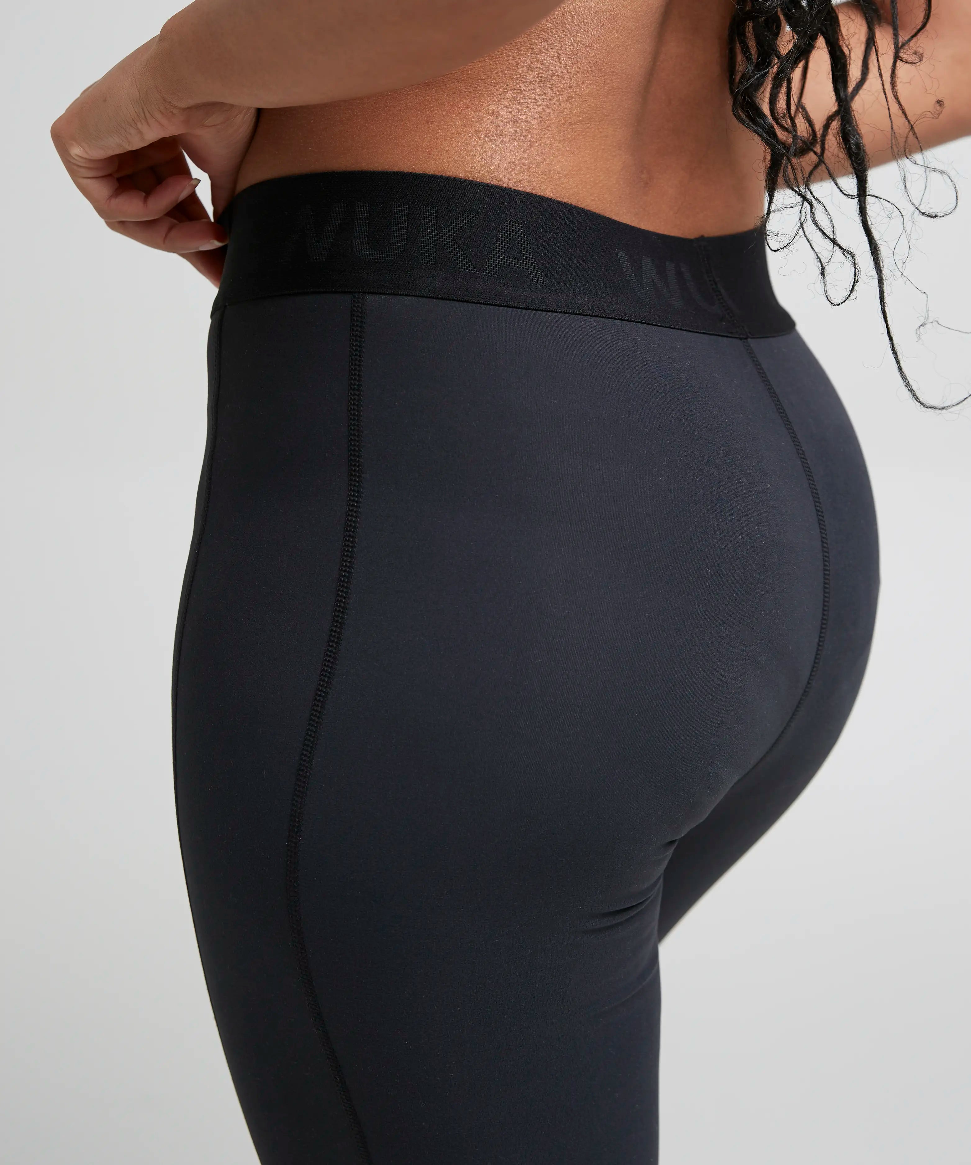 Back of woman wearing the Wuka performance leggings in black showing the elasticated waist band and side pocket