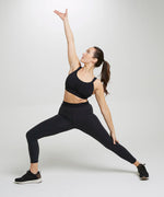 Woman stretching and wearing the Wuka performance leggings in black 