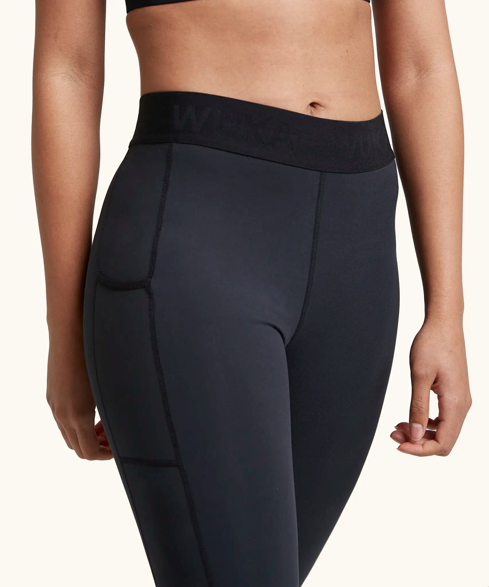 Front of woman wearing the Wuka performance leggings in black showing the elasticated waist band and side pocket