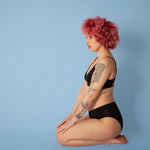Woman on her knees wearing the eco-friendly WUKA reusable seamless midi brief sanitary pants on a blue background