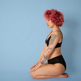 Woman on her knees wearing the eco-friendly WUKA reusable seamless midi brief sanitary pants on a blue background