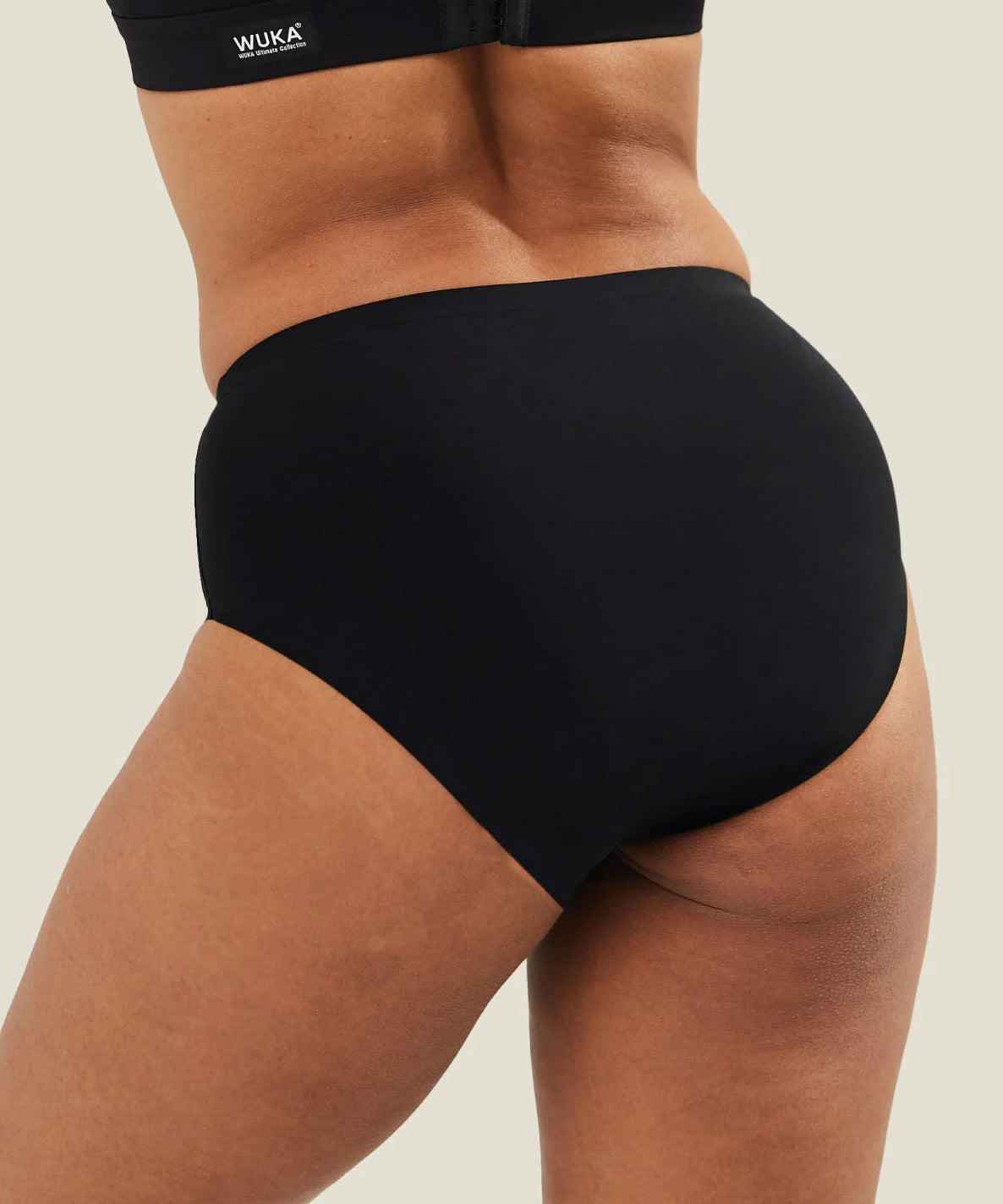Back view of a model wearing black WUKA Stretch™ Seamless Midi Brief period pants, showing full coverage and seamless construction across the back.