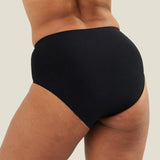 Back view of a model wearing black WUKA Stretch™ Seamless Midi Brief period pants, showing full coverage and seamless construction across the back.