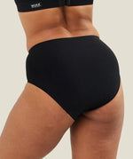 Back view of a model wearing black WUKA Stretch™ Seamless Midi Brief period pants, showing full coverage and seamless construction across the back.