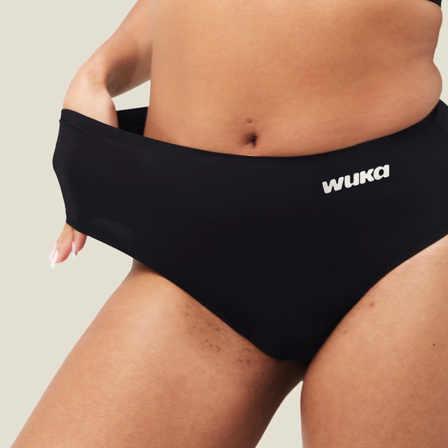 Front view of a model gently stretching the waistband of the WUKA Stretch™ Seamless Midi Brief period pants, showing the flexible, multi-size fit of the microfiber fabric.