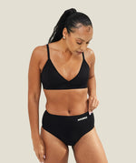Lifestyle image of a model wearing the WUKA Stretch™ Seamless Midi Brief period underwear with a matching black bra, showing the full outfit and how the period pants sit on the body.