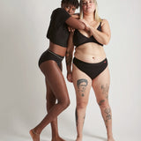 Pair of women wearing the Wuka ultimate bikini style medium flow period brief in black
