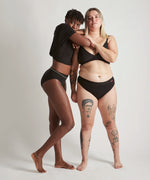 Pair of women wearing the Wuka ultimate bikini style medium flow period brief in black