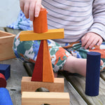 A close up of a child stacking blocks from the Wooden Story Rainbow XL Blocks set on top of each other.