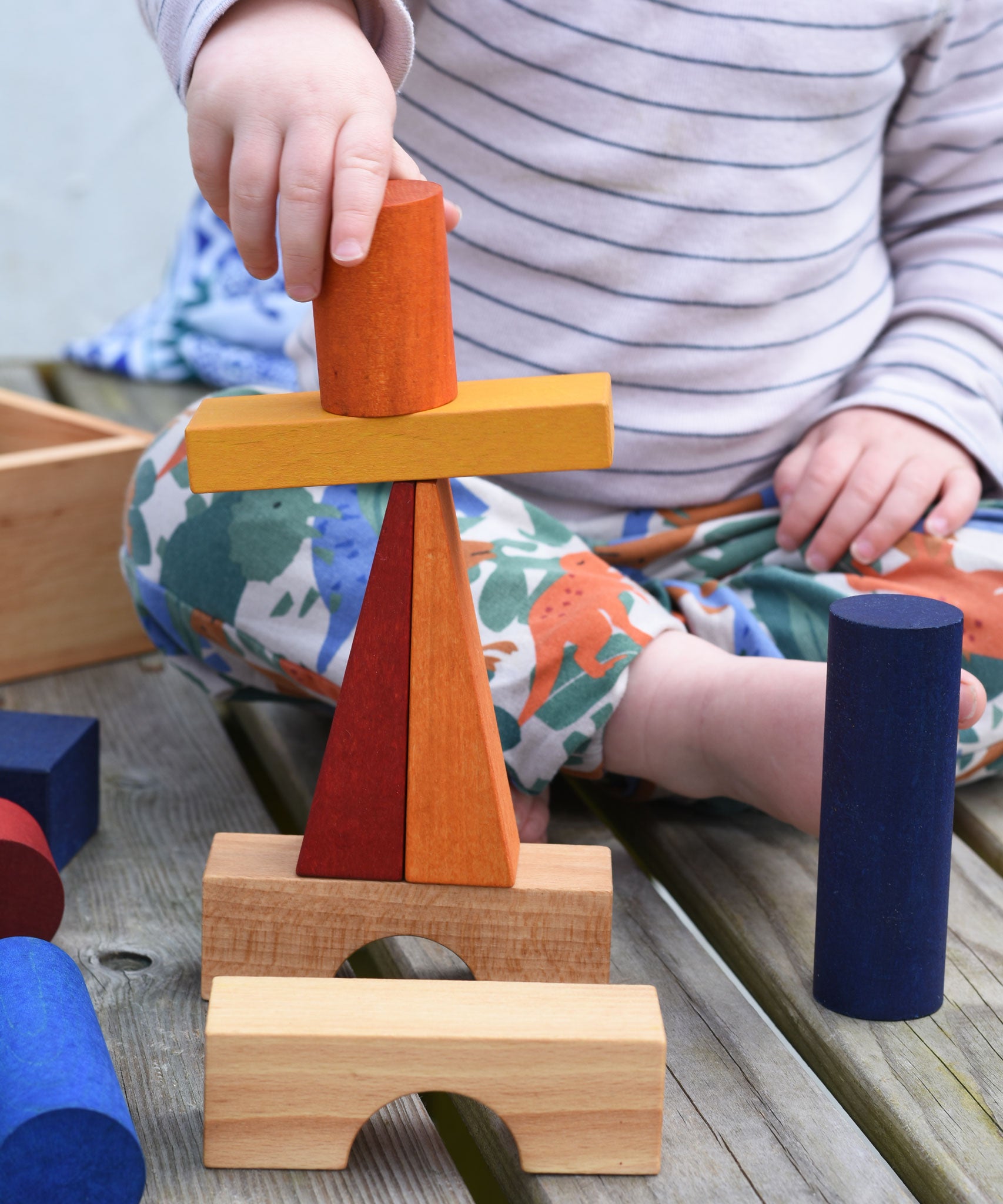 A close up of a child stacking blocks from the Wooden Story Rainbow XL Blocks set on top of each other.