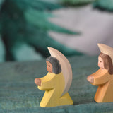 A yellow Ostheimer little angel placed on a green decorative cloth. This wooden figure is part of a large range of expertly hand crafted, Waldorf inspired, wooden toys here at Babipur. 