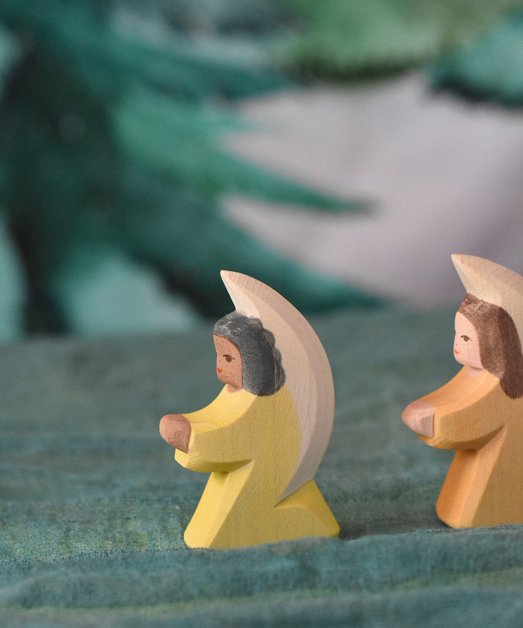 A yellow Ostheimer little angel placed on a green decorative cloth. This wooden figure is part of a large range of expertly hand crafted, Waldorf inspired, wooden toys here at Babipur. 