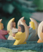 A little yellow angel wooden toy figure from Ostheimer placed on green coloured decorative cloths. Other little angels can be seen in the back. This wooden figure is part of a large range of expertly hand crafted, Waldorf inspired, wooden toys here at Babipur. 