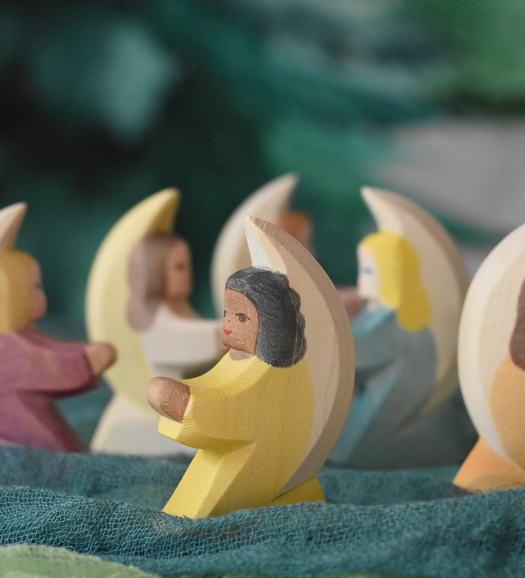 A little yellow angel wooden toy figure from Ostheimer placed on green coloured decorative cloths. Other little angels can be seen in the back. This wooden figure is part of a large range of expertly hand crafted, Waldorf inspired, wooden toys here at Babipur. 