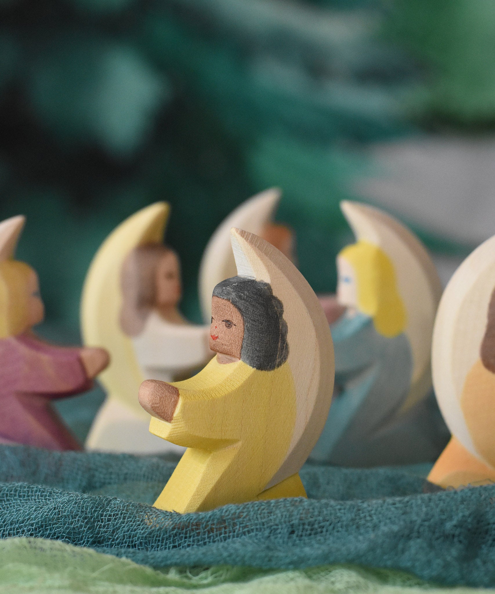 A little yellow angel wooden toy figure from Ostheimer placed on green coloured decorative cloths. Other little angels can be seen in the back. This wooden figure is part of a large range of expertly hand crafted, Waldorf inspired, wooden toys here at Babipur. 