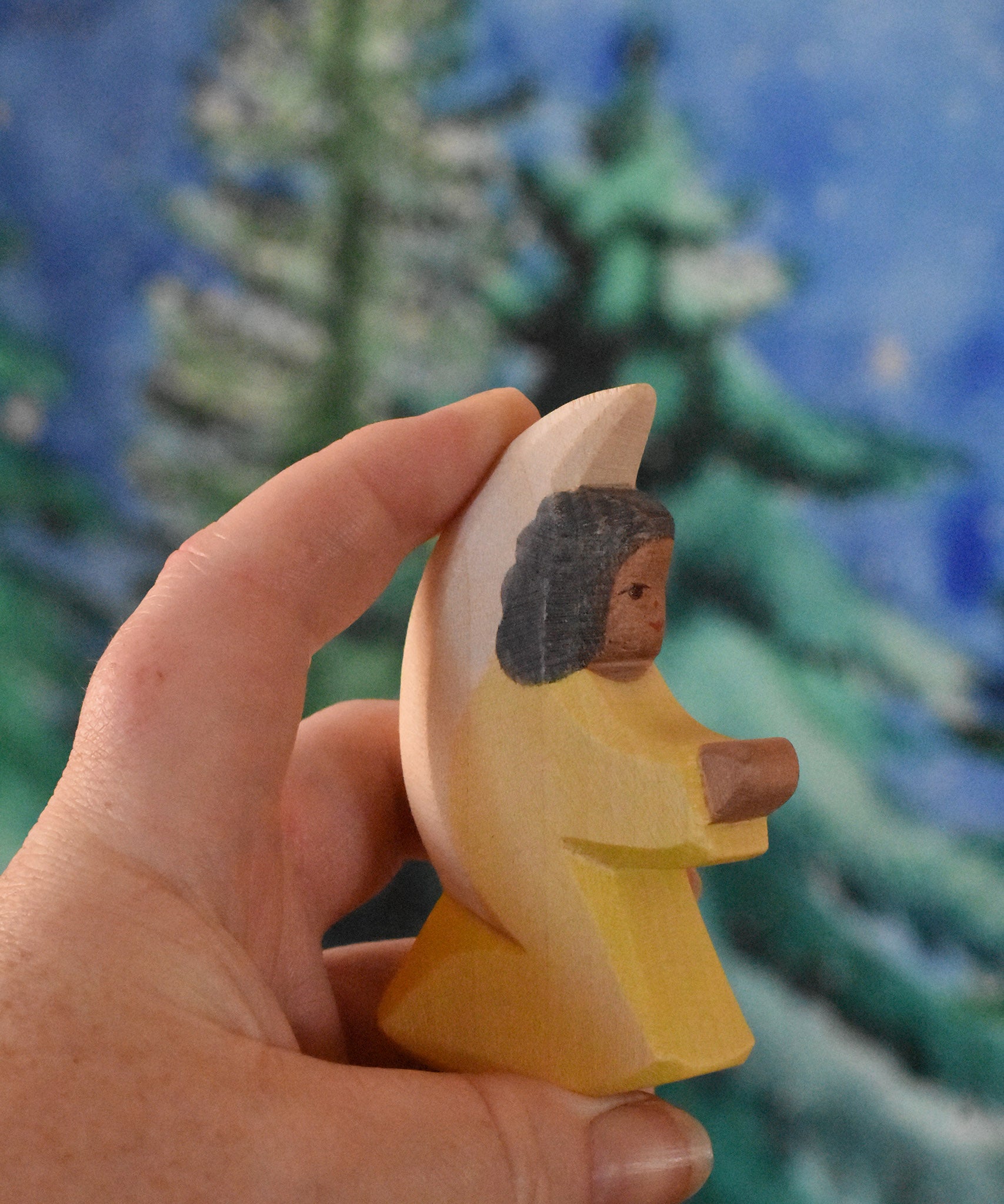 A yellow coloured Ostheimer little angel held in an adult's hand to show scale. This wooden figure is part of a large range of expertly hand crafted, Waldorf inspired, wooden toys here at Babipur. 