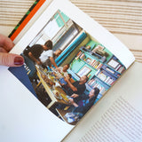 A page from the Zaitoun Palestinian Cookbook by activist and author Yasmin Khan. The images inside show Palestinians sitting around a table and enjoying a traditional middle eastern meal.